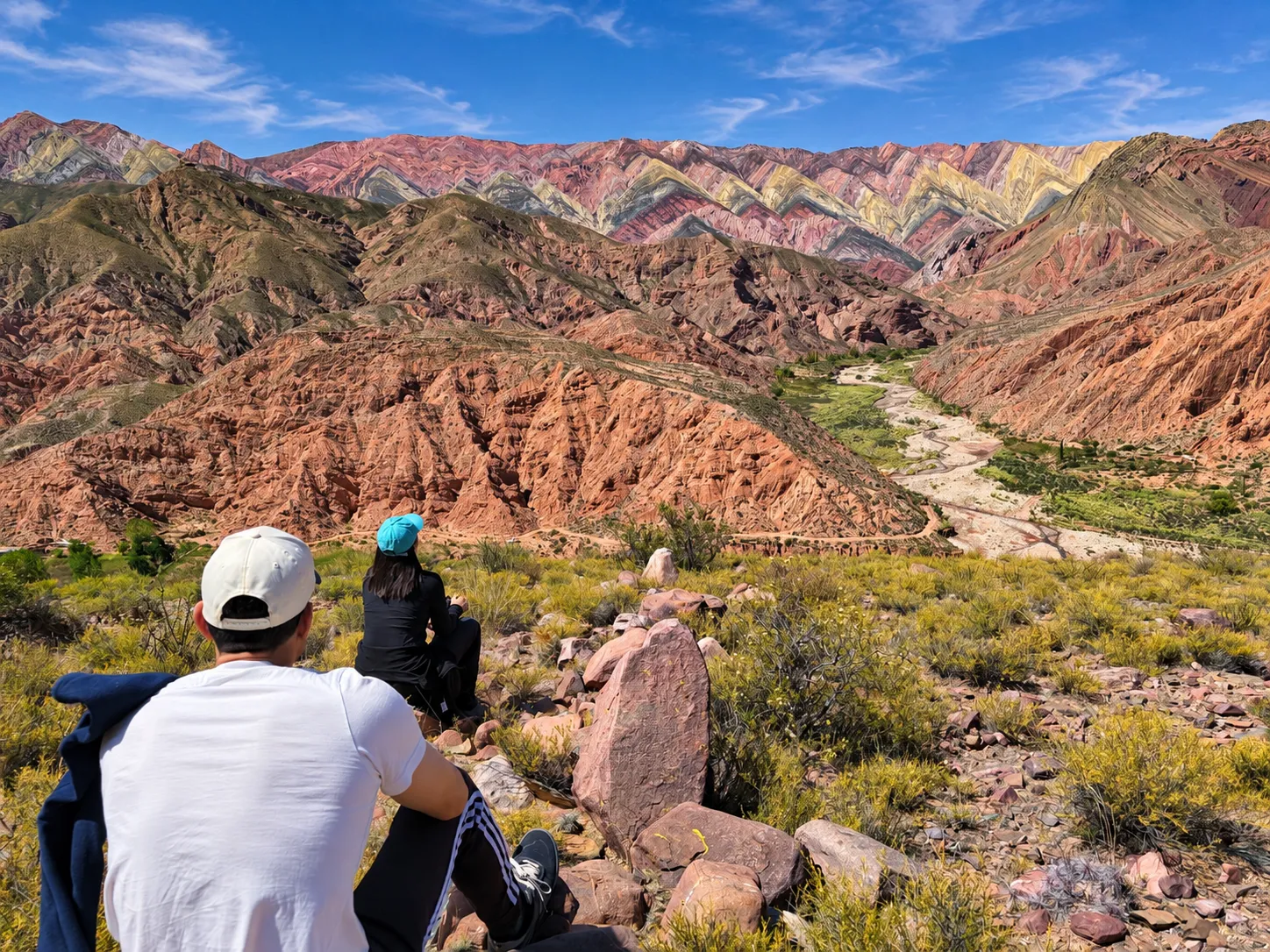Pareja de viajeros sentados frente al Cerro de los 14 Colores en la caminata al Corazón del Hornocal